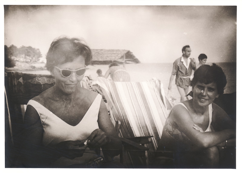 Zwei junge Frauen mit Sonnenbrille sitzen am Strand